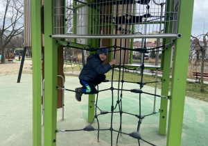 Chłopiec wspina się po sznurkowej drabince na placu zabaw